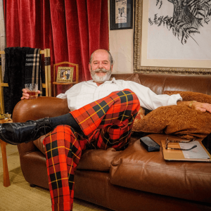 Mark Lewis sitting on sof in tartan trousers